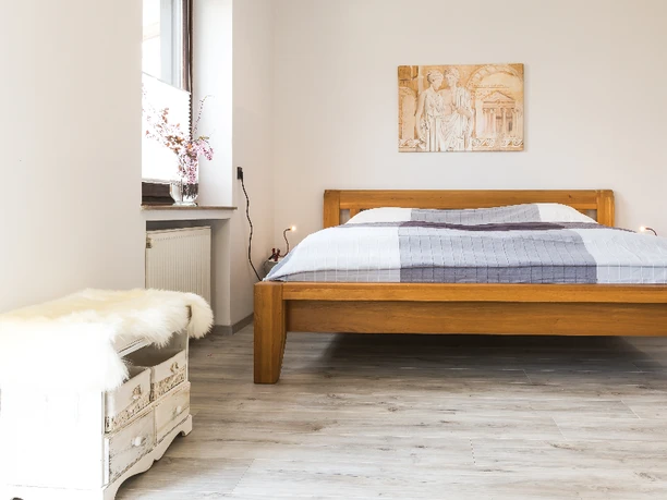 B&B Bultschnieder Helles Schlafzimmer mit Holzbett, weißem Nachttisch und Wandgemälde, Fenster auf der linken Seite.