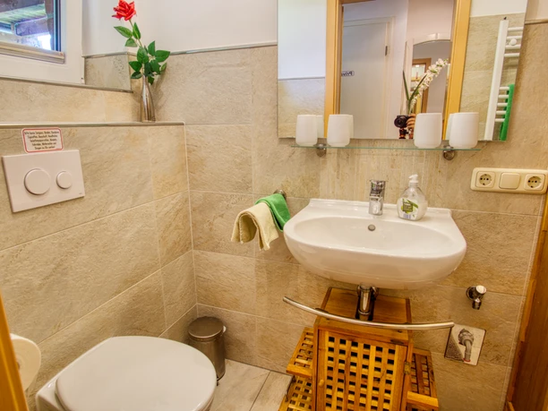 Bad.jpeg Badezimmer mit beigen Fliesen, weißem Waschbecken, Holzunterschrank, Spiegel und Toilette.