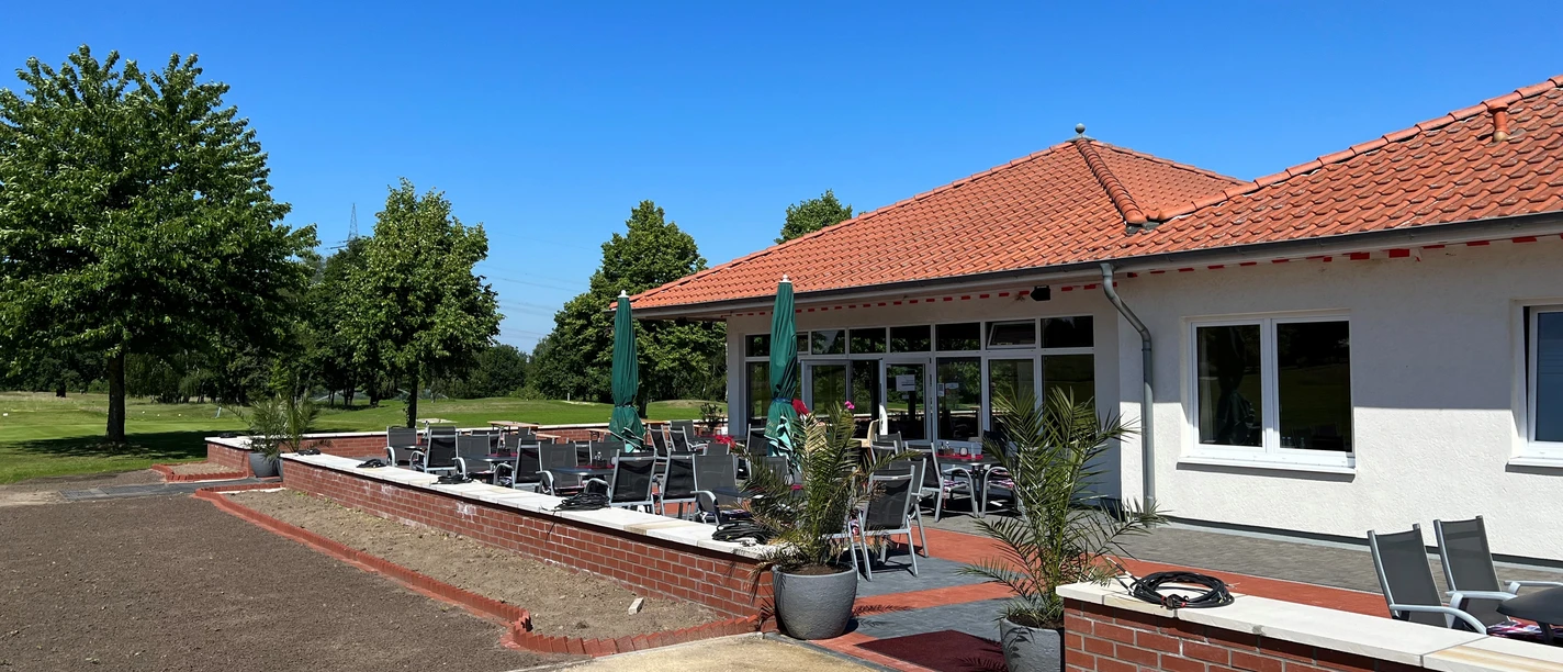 Outdoor terrace of a restaurant on the golf course with red tiles and parasols under a blue sky.