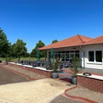 Gastronomie Panorama am Golfplatz Außen Außenterrasse eines Restaurants am Golfplatz mit roten Ziegeln und Sonnenschirmen unter blauem Himmel.Outdoor terrace of a restaurant on the golf course with red tiles and parasols under a blue sky.Udendørs terrasse på en restaurant på golfbanen med røde fliser og parasoller under en blå himmel.Buitenterras van een restaurant op de golfbaan met rode tegels en parasols onder een blauwe hemel.