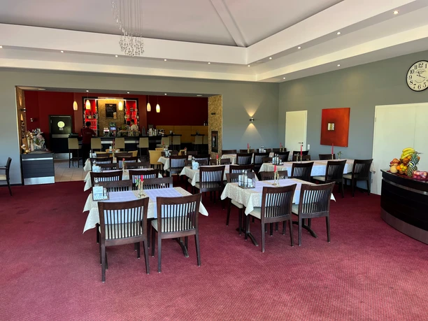 A restaurant with red walls, laid tables and a modern ambience next to a golf course.