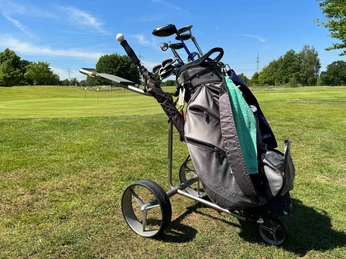 A golf bag with clubs on a golf course in front of a clear blue sky and green trees.