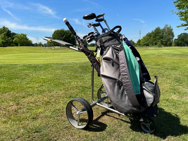 Golftasche A golf bag with clubs on a golf course in front of a clear blue sky and green trees.