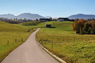 Blick bei Bad Bayersoien Landschaft mit grünen Hügeln, einer Straße und einem Bergpanorama im Hintergrund.