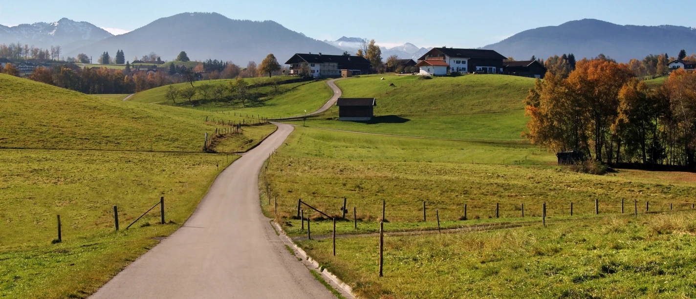 Blick bei Bad Bayersoien Landschaft mit grünen Hügeln, einer Straße und einem Bergpanorama im Hintergrund.