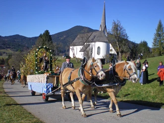 Leonhardiritt Unterammergau Zwei Pferde ziehen einen geschmückten Wagen beim Leonhardiritt in Unterammergau vorbei an einer Kirche.