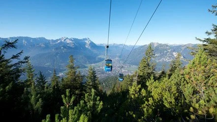 Wankbahn Seilbahn schwebt über bewaldeten Hang mit Alpenblick in der Ferne.