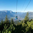 Wankbahn Seilbahn schwebt über bewaldeten Hang mit Alpenblick in der Ferne.