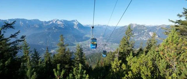 Wankbahn Seilbahn schwebt über bewaldeten Hang mit Alpenblick in der Ferne.