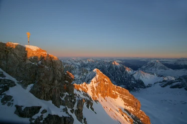 Zugspitzgipfel Verschneiter Gipfel der Zugspitze bei Sonnenuntergang mit schneebedeckten Bergen im Hintergrund.