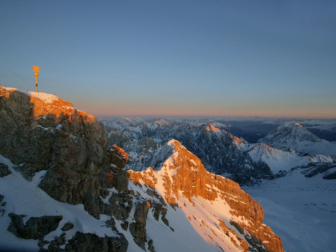 Zugspitzgipfel Verschneiter Gipfel der Zugspitze bei Sonnenuntergang mit schneebedeckten Bergen im Hintergrund.