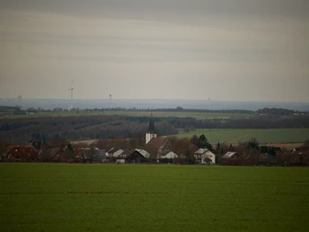 Dorfansicht von Dörenhagen mit Kirchturm im Zentrum, umgeben von sanften Hügeln und Windkraftanlagen.