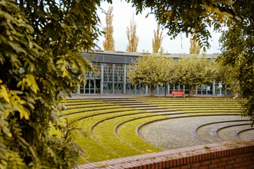 Ringlokschuppen, Mülheim a. d. Ruhr <p>Moderner, überdachter Platz mit halbrunden Sitzstufen und Ziegelwand, umrahmt von Bäumen.</p>