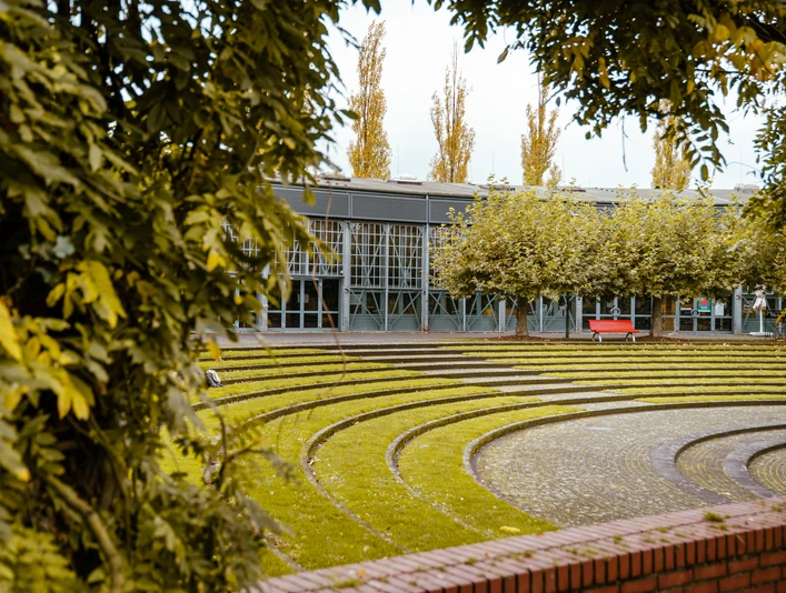 Ringlokschuppen, Mülheim a. d. Ruhr <p>Moderner, überdachter Platz mit halbrunden Sitzstufen und Ziegelwand, umrahmt von Bäumen.</p>