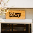 Bohnen Kartell in Rüttenscheid, Essen <p>Holzschild "Bohnen Kartell" über einer modernen Fassade, Baum mit zarten Blüten im Vordergrund.</p>