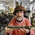 Die Buchmacherey in Velbert-Langenberg mit Hans Josef Altmann.jpg Ein Buchdrucker in traditioneller Kleidung hält eine Druckplatte in einer historischen Werkstatt.