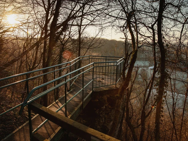 Aussichtspunkt Teufelsstein oberhalb des Paddelteiches Etteln Metallplattform mit seitlichen Geländern in einem Waldgebiet, bietet Blick auf einen See bei Sonnenuntergang.
