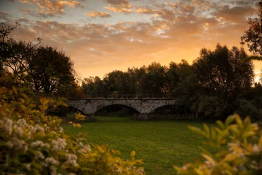 Nordborchen Viadukt Steinbogenviadukt von Bäumen umrahmt, beleuchtet von warmen Farben eines Sonnenuntergangs am ruhigen Himmel.