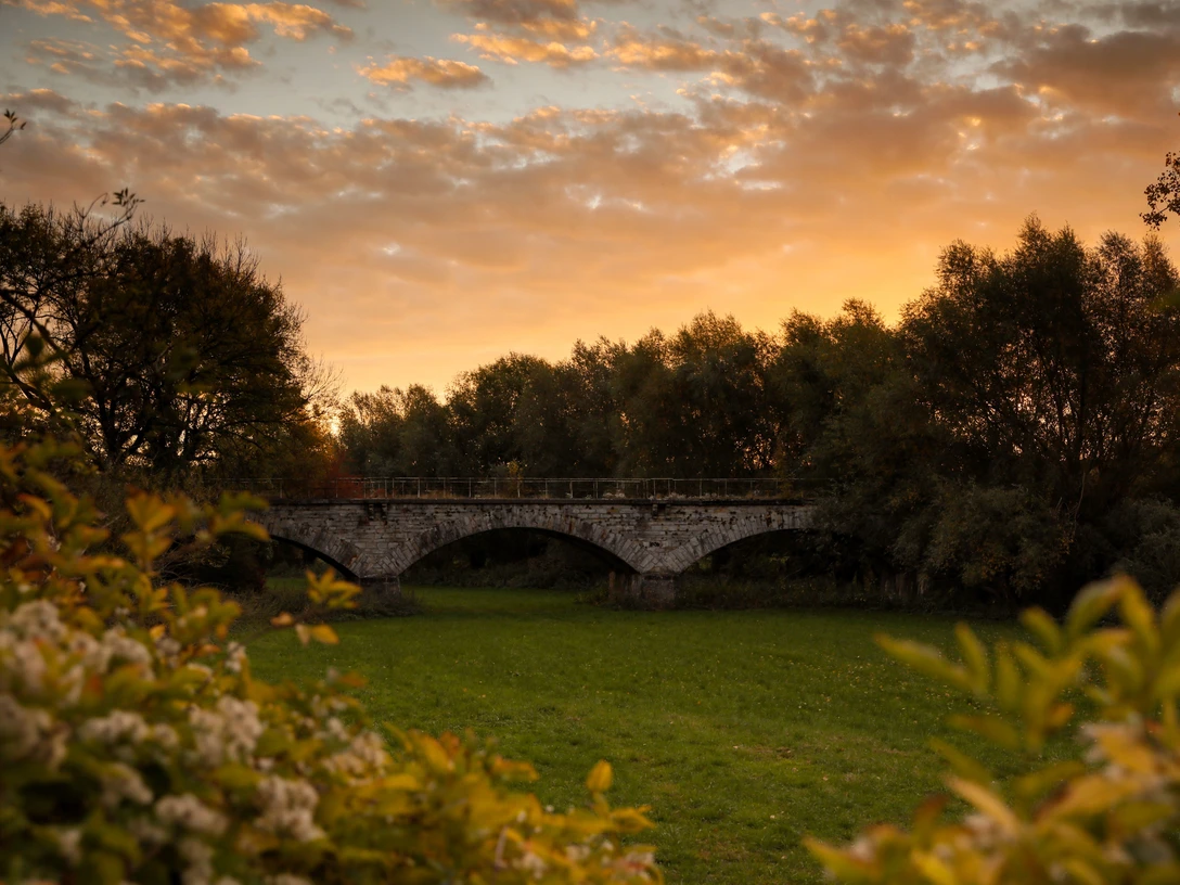 Nordborchen Viadukt Steinbogenviadukt von Bäumen umrahmt, beleuchtet von warmen Farben eines Sonnenuntergangs am ruhigen Himmel.