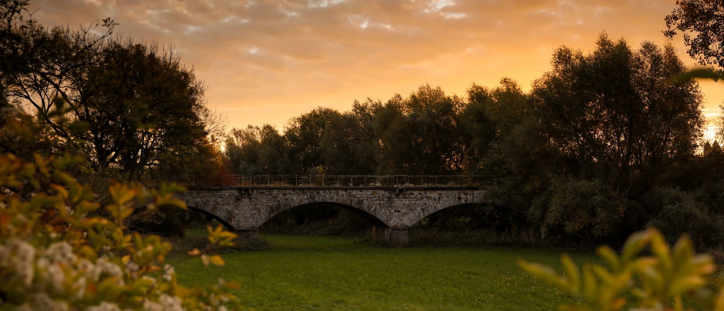 Nordborchen Viadukt Steinbogenviadukt von Bäumen umrahmt, beleuchtet von warmen Farben eines Sonnenuntergangs am ruhigen Himmel.