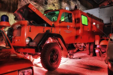 Feuerwehrmuseum Heiligenhaus Ein leuchtend rotes historisches Feuerwehrfahrzeug parkt unter einem stimmungsvoll ausgeleuchteten Vordach.