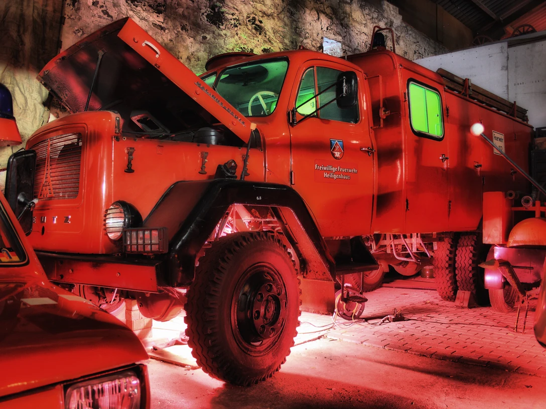 Feuerwehrmuseum Heiligenhaus Ein leuchtend rotes historisches Feuerwehrfahrzeug parkt unter einem stimmungsvoll ausgeleuchteten Vordach.