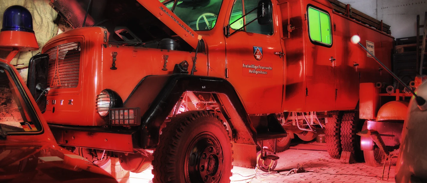 Feuerwehrmuseum Heiligenhaus Ein leuchtend rotes historisches Feuerwehrfahrzeug parkt unter einem stimmungsvoll ausgeleuchteten Vordach.