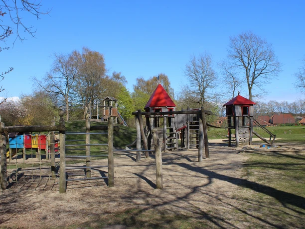 Spielplatz Cadenberge Holzspielplatz mit Klettergerüsten, Rutschen und Türmen im Grünen unter blauem Himmel in Cadenberge.