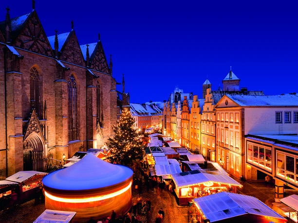 Weihnachtsmarkt in winterlicher Atmosphäre mit hell erleuchteten Ständen und einer historischen Kirche.