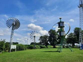 Grüne Wiese mit historischen Windkraftanlagen und blauem Himmel im Deutschen Windkraftmuseum.
