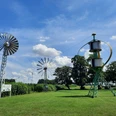 Grüne Wiese mit historischen Windkraftanlagen und blauem Himmel im Deutschen Windkraftmuseum.