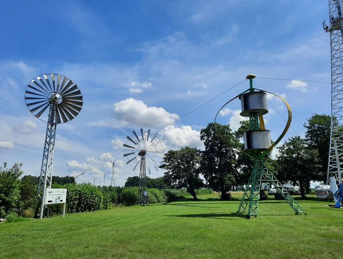 Deutsches Windkraftmuseum e.V. Grüne Wiese mit historischen Windkraftanlagen und blauem Himmel im Deutschen Windkraftmuseum.