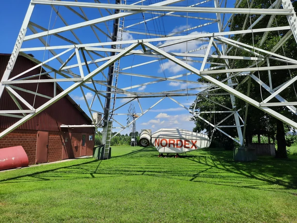 Metallkonstruktion des Deutschen Windkraftmuseums in sonniger, grüner Umgebung mit Nordex-Windrad.