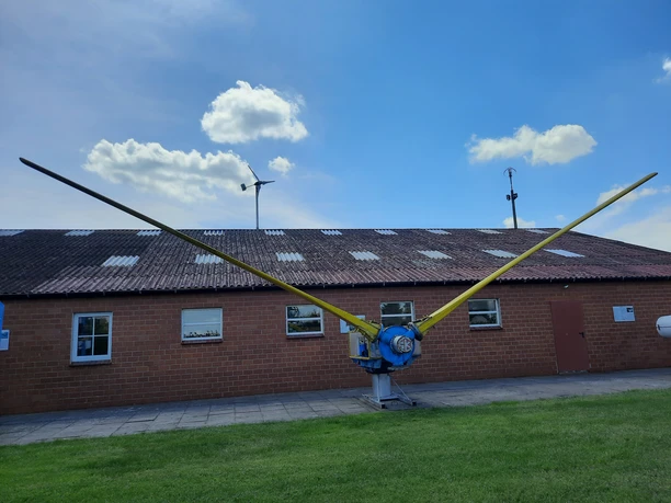 Deutsches Windkraftmuseum e.V. Große Windkraftanlage mit gelben Rotorblättern vor einem Backsteingebäude unter blauem Himmel.