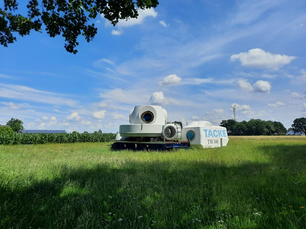 Deutsches Windkraftmuseum e.V. Windkraftanlage in einer grünen Wiese, umgeben von Baumwipfeln, zeigt technische Details.