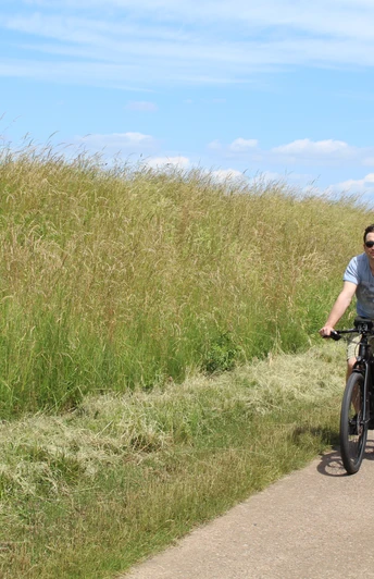 Zwei Personen, die auf einem asphaltierten Weg durch eine grüne, ländliche Landschaft radeln.