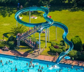 Heljensbad in Heiligenhaus Ein Freibad mit einer geschwungenen blauen Wasserrutsche, umgeben von einer grünen Liegewiese.