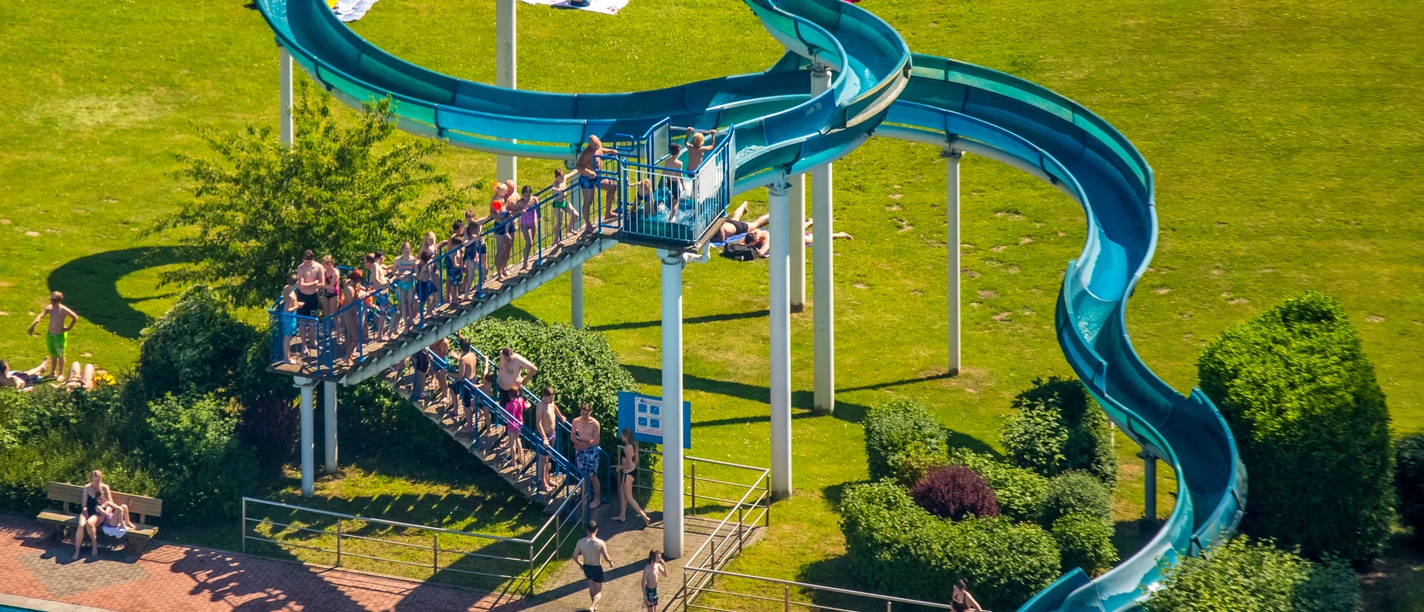 Heljensbad in Heiligenhaus Ein Freibad mit einer geschwungenen blauen Wasserrutsche, umgeben von einer grünen Liegewiese.