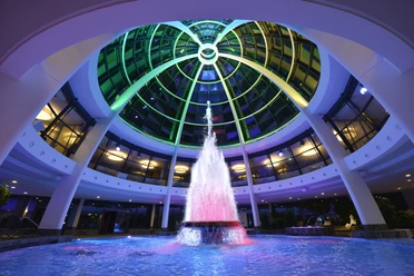 Kuppel der carpesol Spa Therme Colored fountain under an illuminated domed roof in a modern building.