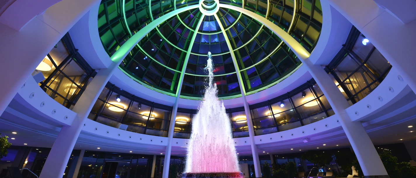 Kuppel der carpesol Spa Therme Colored fountain under an illuminated domed roof in a modern building.