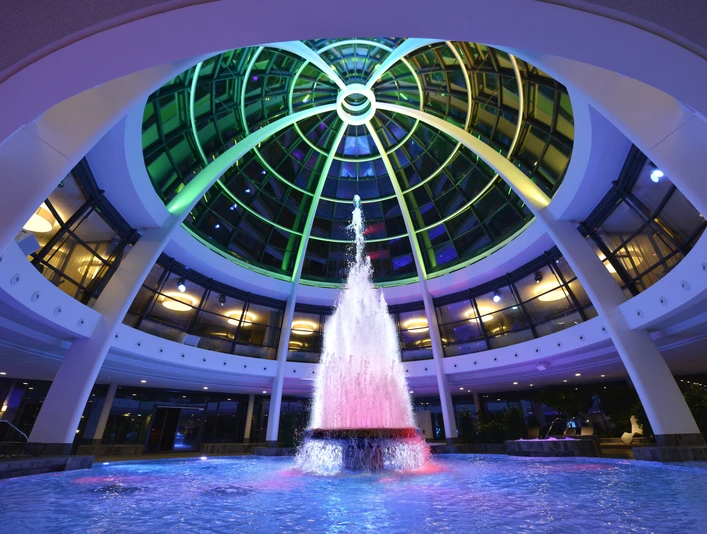Kuppel der carpesol Spa Therme Farbiger Springbrunnen unter beleuchtetem Kuppeldach im modernen Gebäude.Colored fountain under an illuminated domed roof in a modern building.Farvet springvand under et oplyst kuppeltag i en moderne bygning.Gekleurde fontein onder een verlicht koepeldak in een modern gebouw.