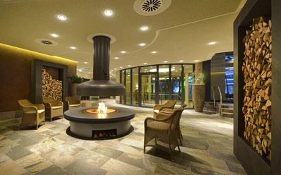 Entspannungsbereiche in der carpesol SPA Therme Gemütlicher Loungebereich mit zentralem Kamin, umgeben von Steinsitzen und Holzstapeln.