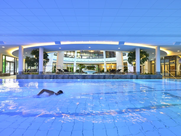 Sportbecken in der carpesol SPA Therme Zwem in het grote, blauw verlichte, moderne binnenzwembad met planten en zithoek.