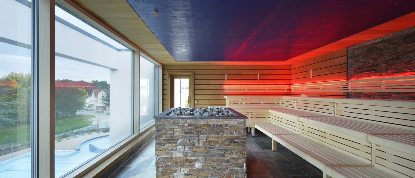 Große Saunalandschaft in der carpesol SPA Therme Moderne sauna met panoramische ramen, houten banken en sfeervolle LED-verlichting.