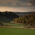 Ein Blick auf Etteln Grüne hügelige Landschaft mit Wäldern; am Horizont ein Dorf und sanfte Schatten der Abenddämmerung.