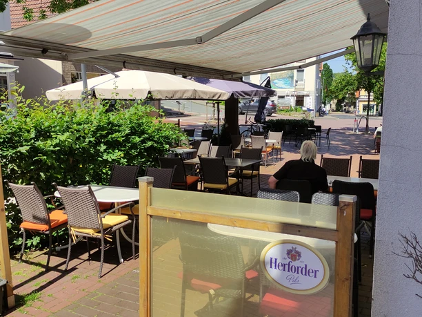 Der Außenbereich eines Cafés mit Holzmöbeln, gemütlichen Sitzgelegenheiten und einem großen Sonnenschirm.
