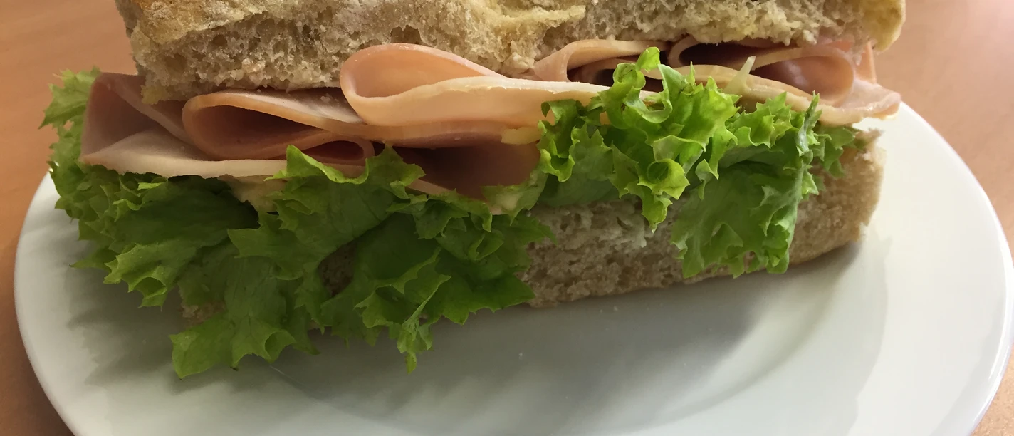 Een vers broodje met sappige ham en knapperige salade geserveerd op een wit bord.