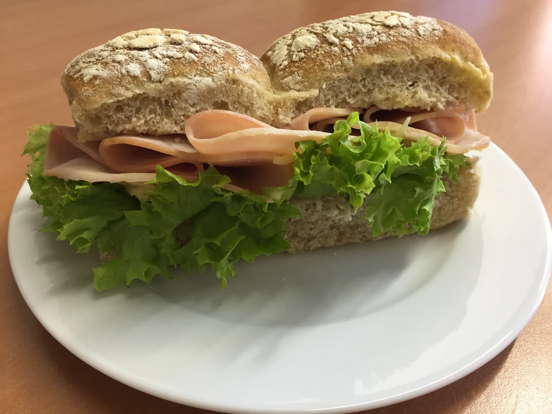 Belegtes Brötchen Ein frisches Brötchen mit saftigem Schinken und knackigem Salat auf einem weißen Teller serviert.