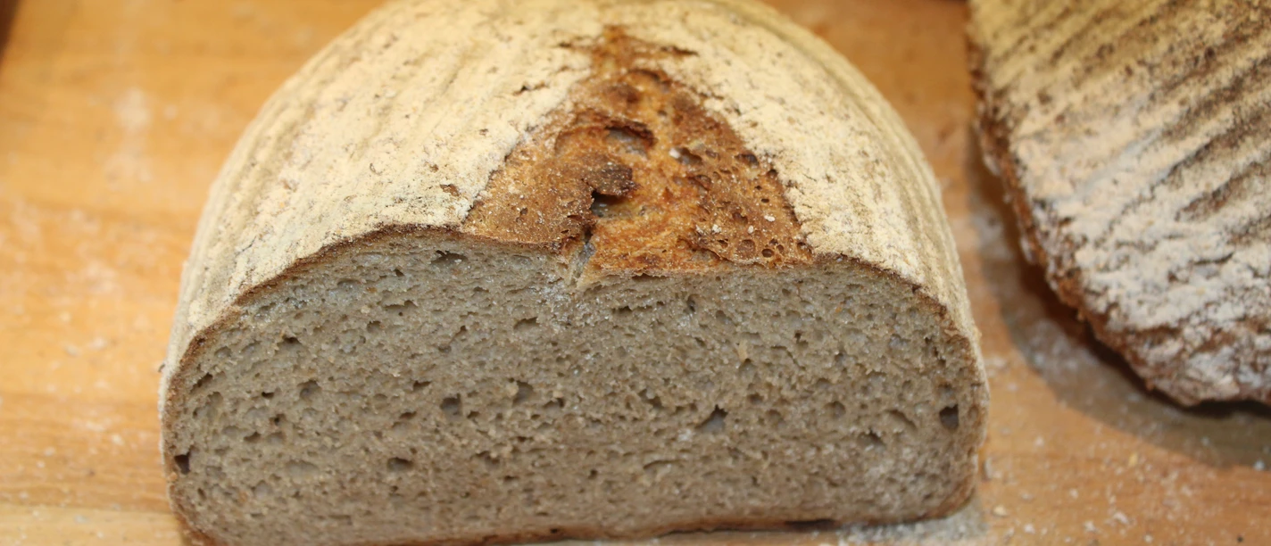 A slice of grainy wholemeal bread lies on a wooden board, surrounded by flour crumbs.