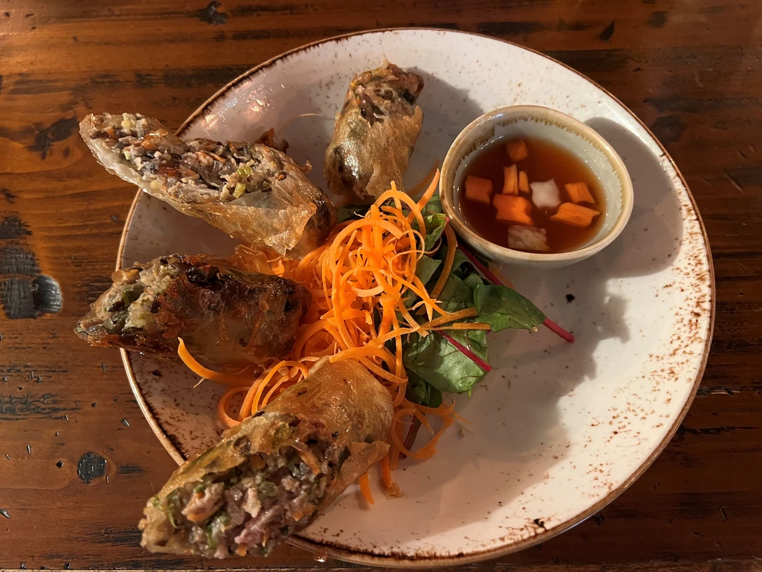 asiatisches Gericht Frühlingsrollen mit einer goldbraunen Kruste, serviert mit frischem Salat und Würzsauce.